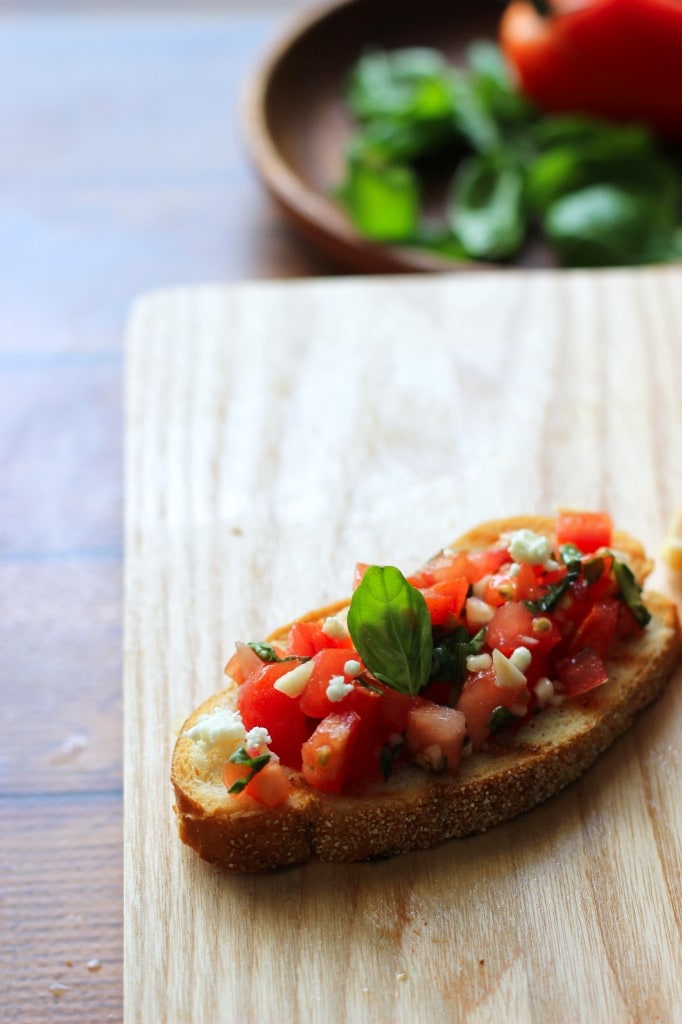 A healthy appetizer of grilled baguette slices rubbed with fresh garlic and topped with tomatoes, garlic, basil and crumbled feta cheese.