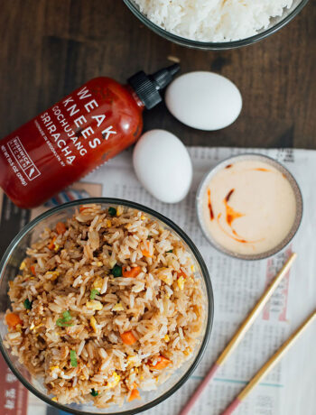 A top down shot of a hibachi-style fried rice with yum yum sauce with chopsticks, eggs, sriracha sauce and white rice.