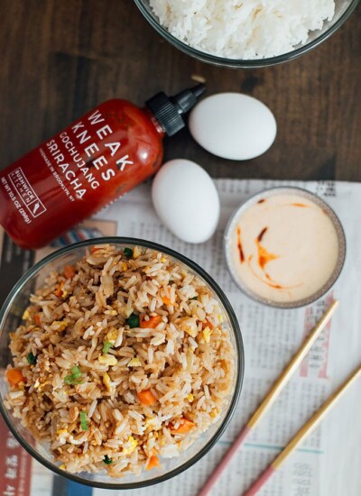 A top down shot of a hibachi-style fried rice with yum yum sauce with chopsticks, eggs, sriracha sauce and white rice.