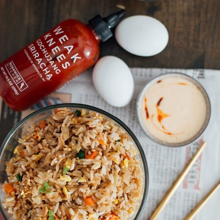 A top down shot of a hibachi-style fried rice with yum yum sauce with chopsticks, eggs, sriracha sauce and white rice.