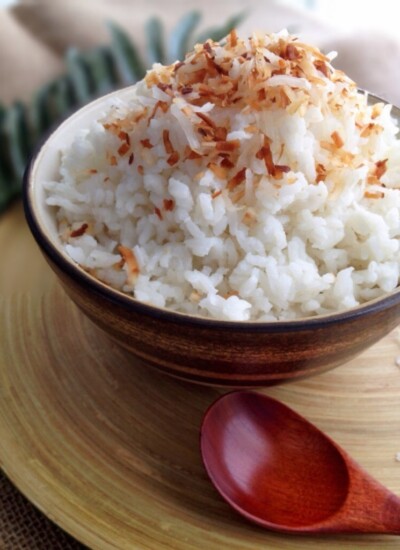 Easy coconut rice in a brown bowl topped with toasted coconut flakes.