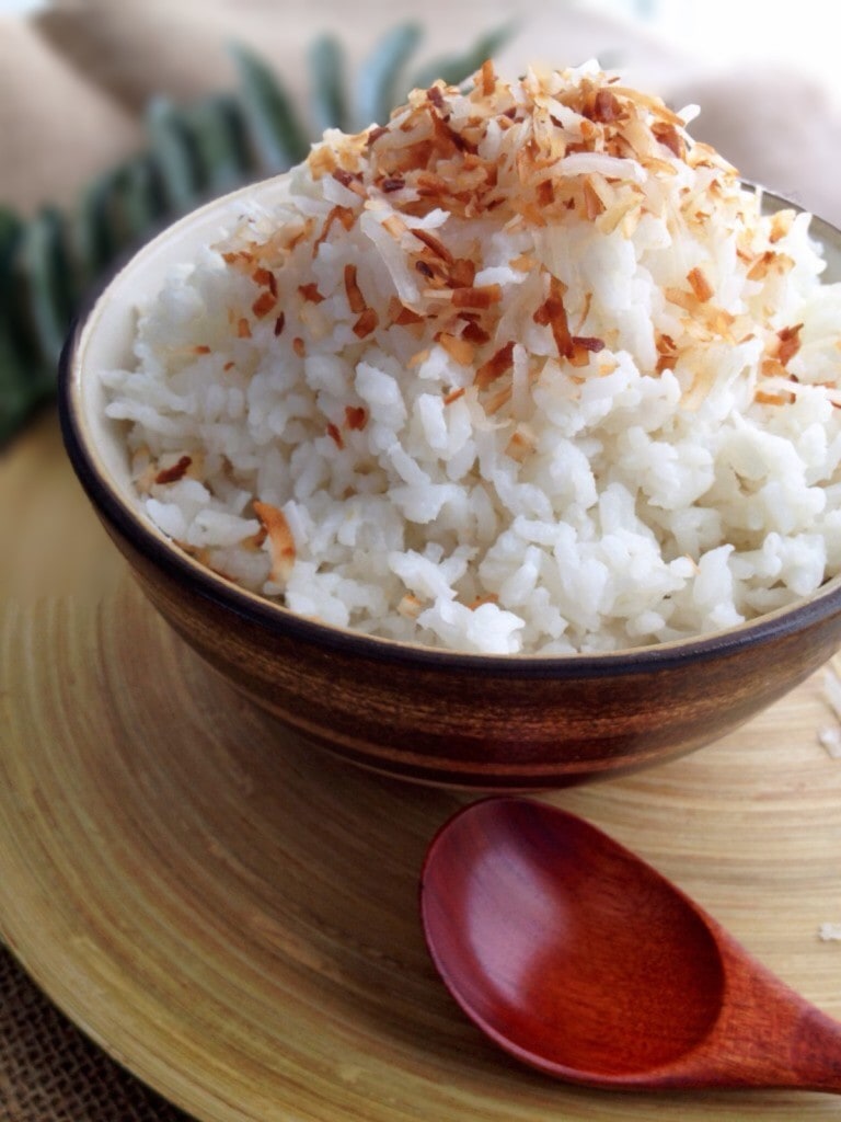 Easy coconut rice in a brown bowl topped with toasted coconut flakes.