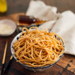 A bowl of messy hibachi noodles topped with sesame seeds and chopsticks on the table.