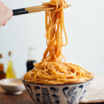 Some chopsticks lifting up messy noodles from a bowl overflowing with hibachi noodles.