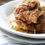 Crispy honey garlic chicken stacked on top of a white plate.