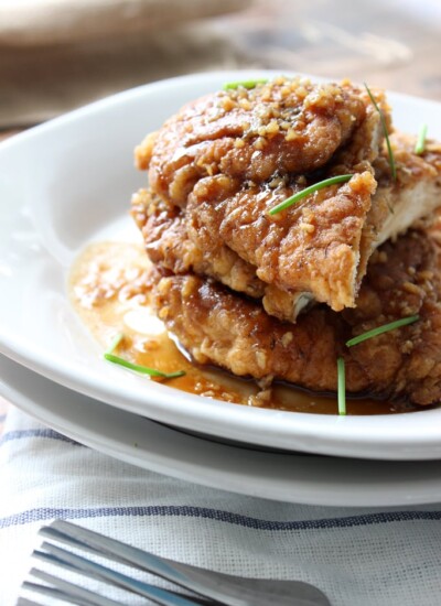 Crispy honey garlic chicken stacked on top of a white plate.