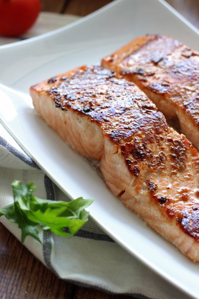 Two honey garlic salmon fillets on a white plate.