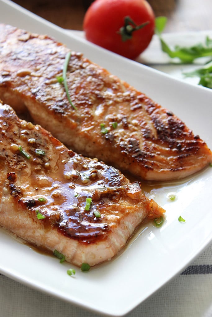 A close up shot of two honey garlic salmon fillets on a white plate.