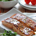 Two fillets of honey garlic salmon on a white plate.