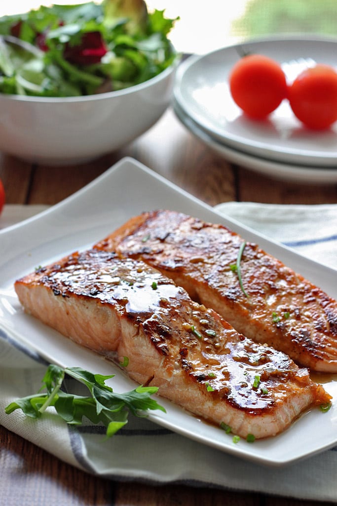 Two honey garlic salmon fillets on a white plate.