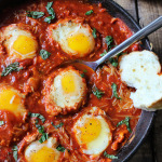 Several sunny side up eggs in marinara sauce topped with basil.