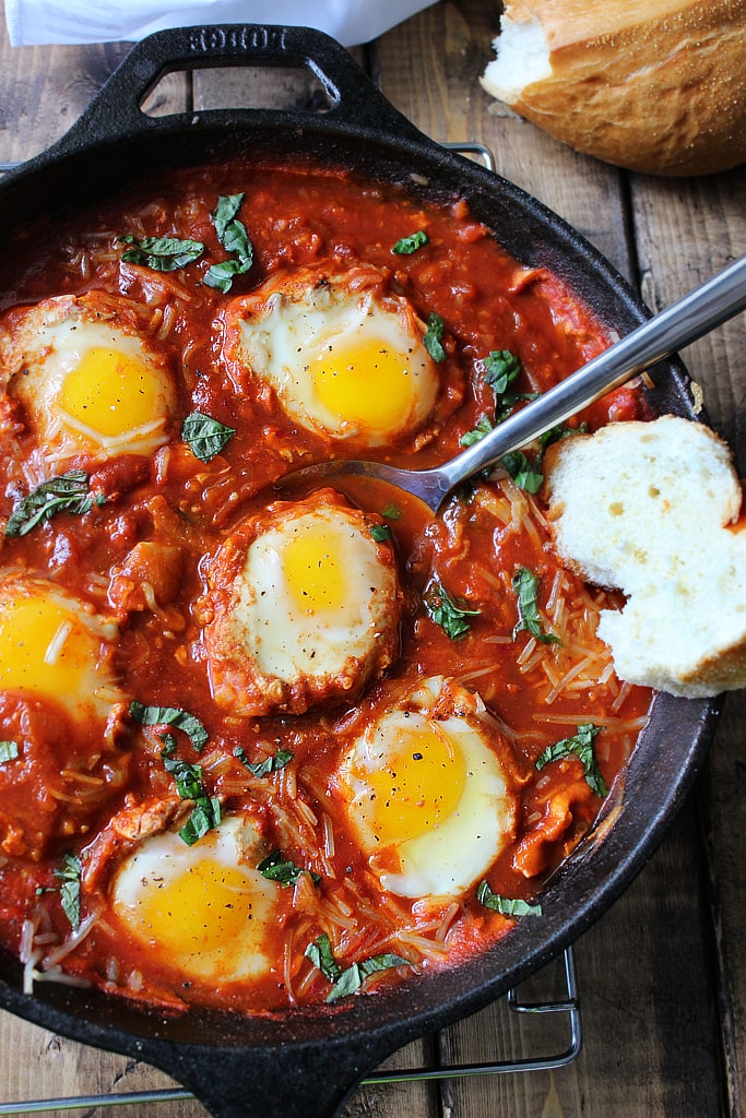 Several sunny side up eggs in marinara sauce topped with basil.