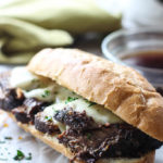 A hearty slow cooker French dip sandwich on white parchment paper with a bowl of au jus dip.