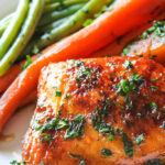 Slow cooker honey garlic chicken thighs on a white plate with carrots and green beans.