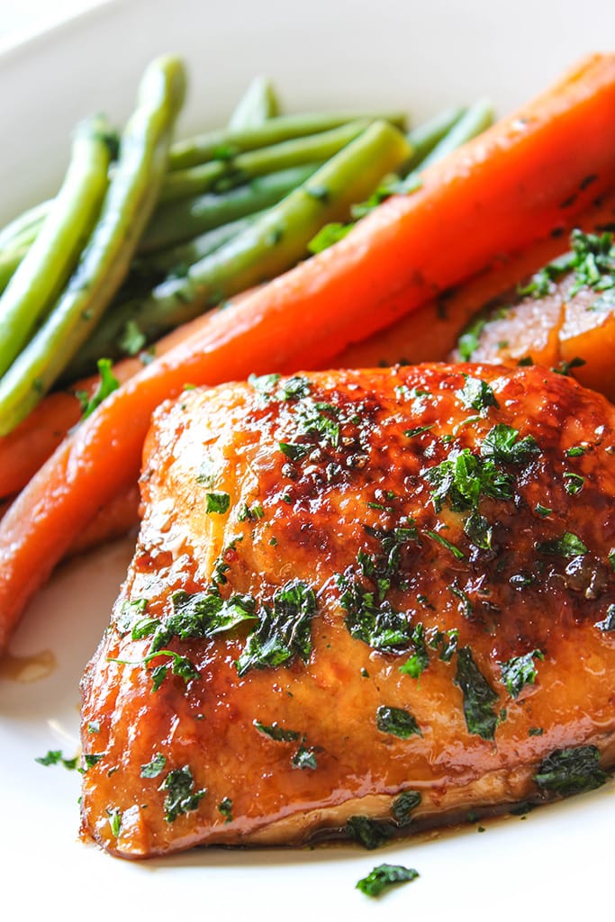 Slow cooker honey garlic chicken thighs on a white plate with carrots and green beans.