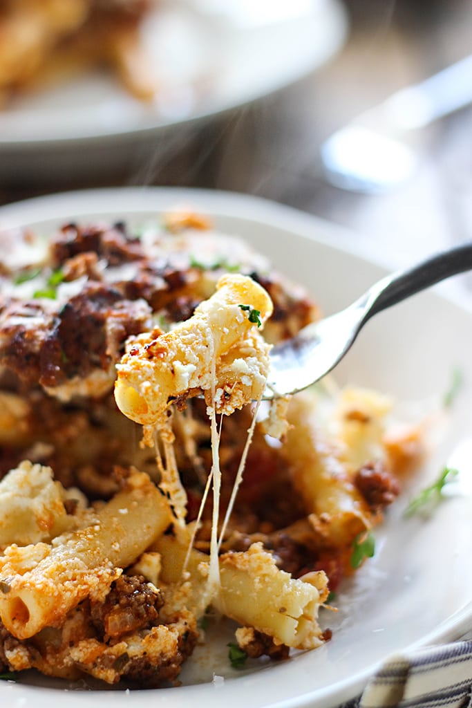 A plate of pasta with cheese strings on a fork.