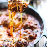 A cheesy meatball lifted from a cast iron skillet with lots of cheese strings.