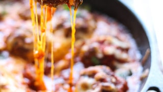 A cheesy meatball lifted from a cast iron skillet with lots of cheese strings.
