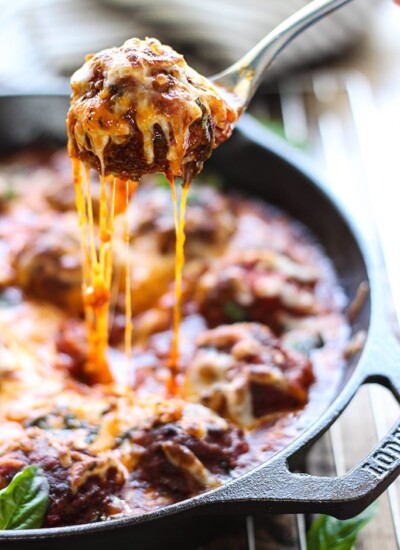 A cheesy meatball lifted from a cast iron skillet with lots of cheese strings.