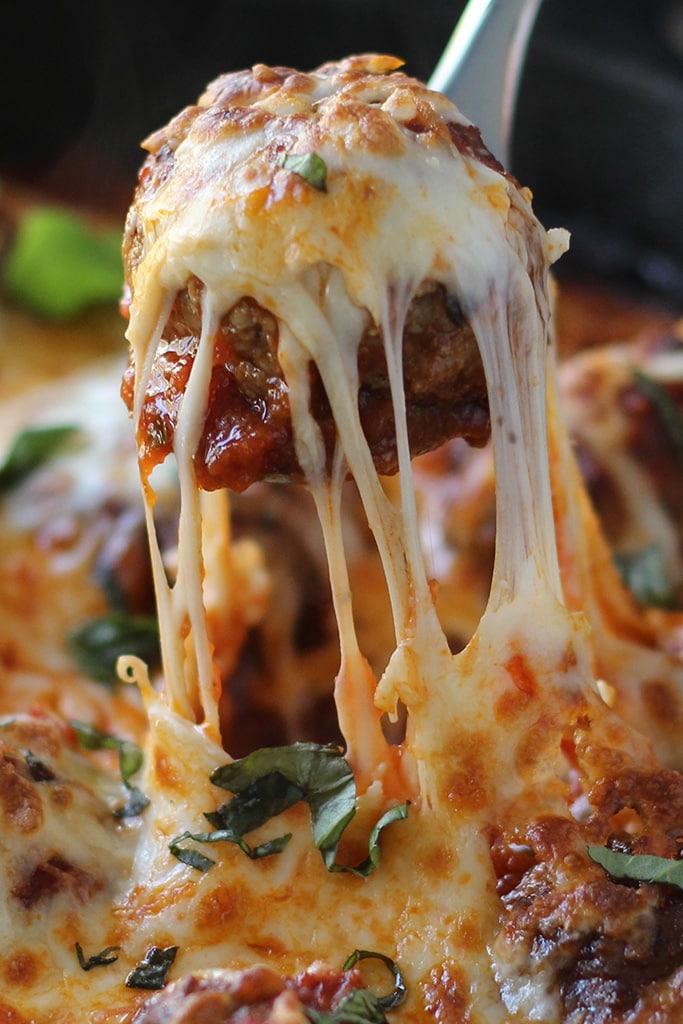 Close up shot of a meatball being lifted up with a spoon with lots of cheese strings.