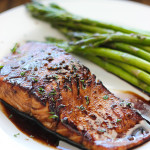 Balsamic glazed salmon on a white plate with some asparagus.