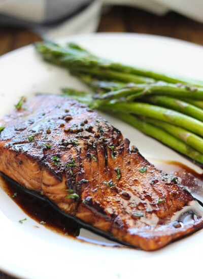 Balsamic glazed salmon on a white plate with some asparagus.