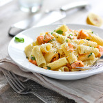 A plate of salmon pasta with fresh basil and lemon wedges.