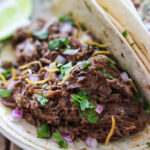 Several corn tacos with shredded beef and toppings.