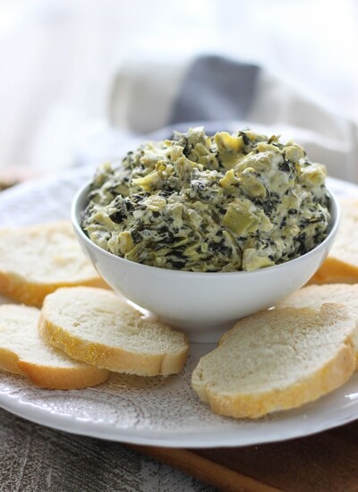 Slow cooker spinach and artichoke dip on a white plate surrounded by sliced French bread.