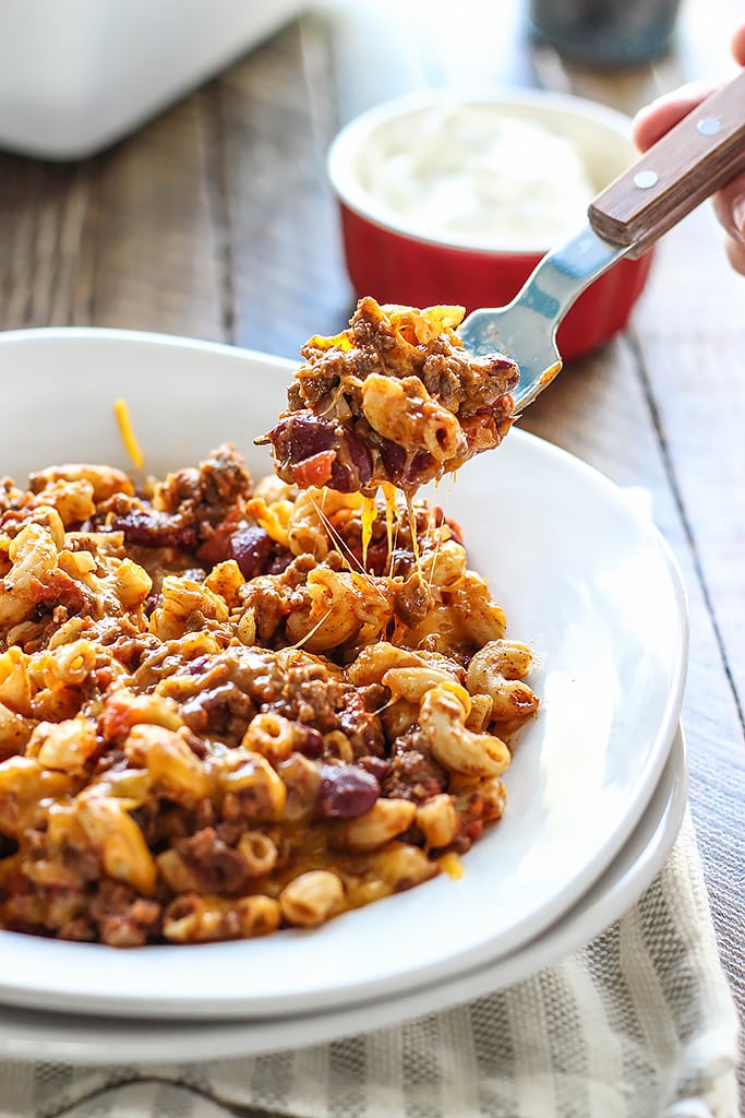 Chili mac and cheese on a white plate lifted on a fork with cheese strings.