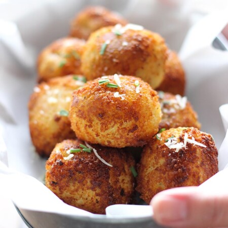 Several stacked loaded mashed potato balls in a bowl covered in white parchment paper.