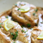 Chicken with lemon garlic cream sauce in a white saucepan topped with parsley and lemon slices.