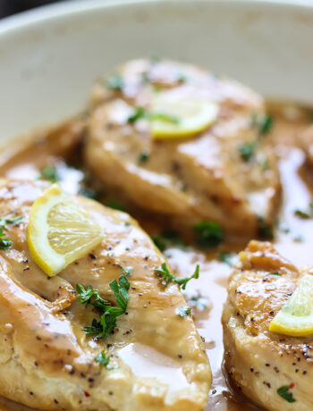 Chicken with lemon garlic cream sauce in a white saucepan topped with parsley and lemon slices.