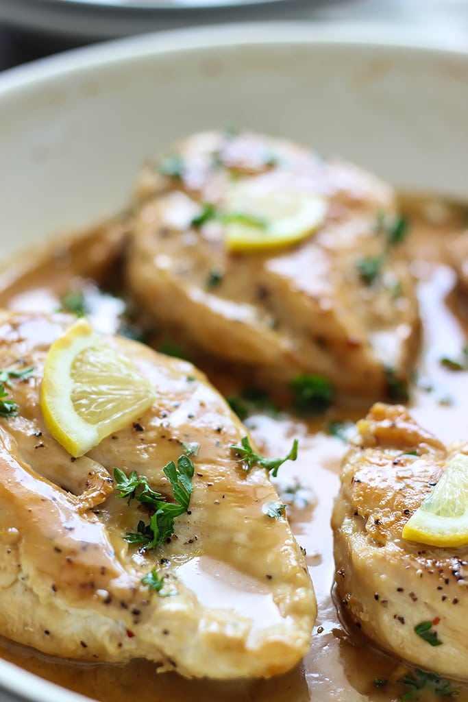 Chicken with lemon garlic cream sauce in a white saucepan topped with parsley and lemon slices.