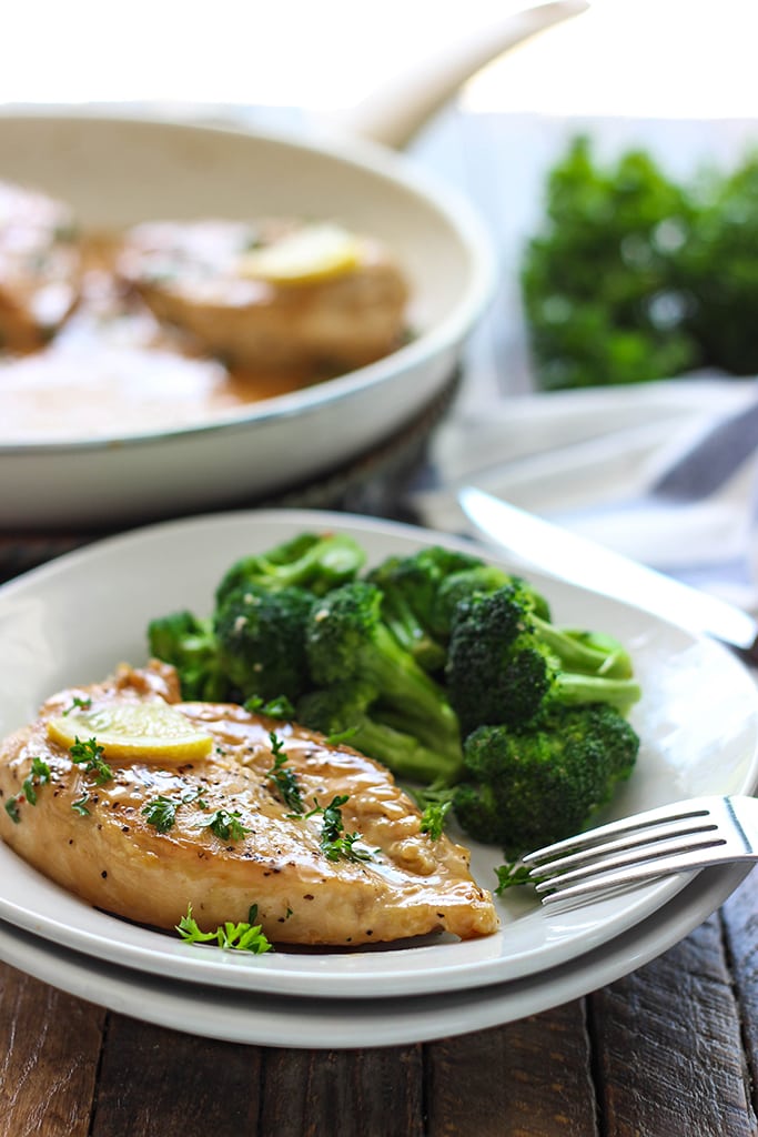 A chicken breast with lemon garlic cream sauce on a white plate with a side of fresh broccoli.