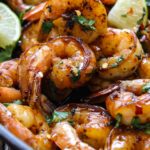 Cilantro lime honey garlic shrimp in a cast iron pan with lime wedges and topped with fresh parsley.