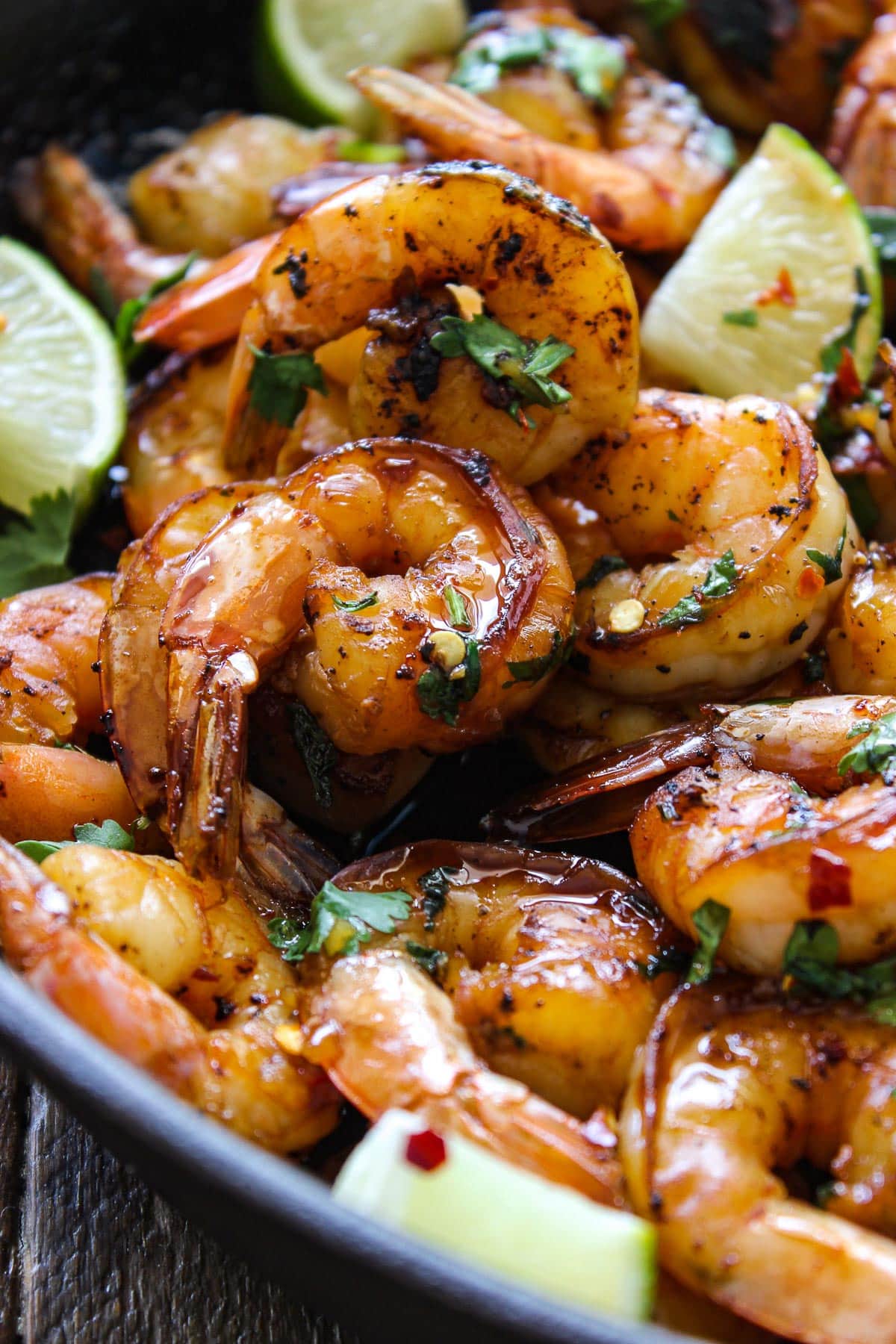 Cilantro lime honey garlic shrimp in a cast iron pan with lime wedges and topped with fresh parsley.