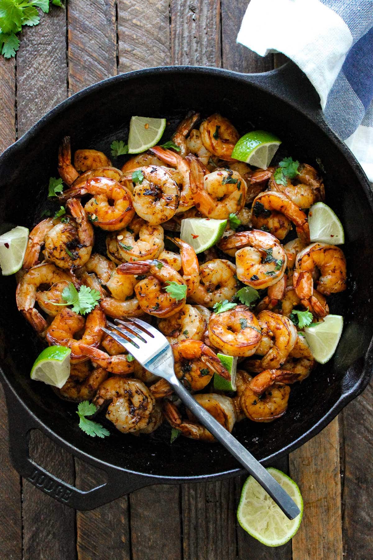 Cilantro lime honey garlic shrimp in a cast iron pan with lime wedges and topped with fresh parsley.