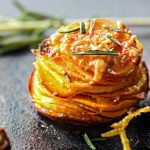 A sweet potato stack on a black cutting board with fresh rosemary.