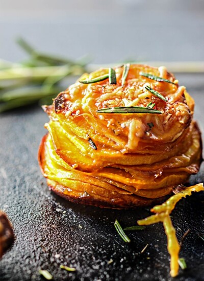 A sweet potato stack on a black cutting board with fresh rosemary.