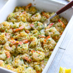 A white casserole dish with lemon garlic butter baked shrimp topped with fresh parsley.