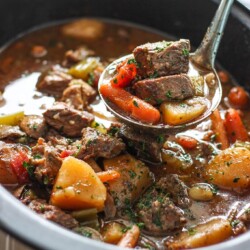 Slow cooker beef stew in a slow cooker with chunks of chuck roast, potatoes and carrots topped with fresh parsley.