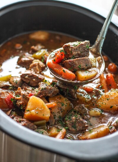 Slow cooker beef stew in a slow cooker with chunks of chuck roast, potatoes and carrots topped with fresh parsley.