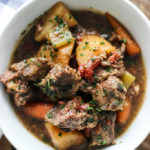 Slow cooker beef stew in a white bowl with chunks of chuck roast, potatoes and carrots topped with fresh parsley.