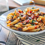 Pepperoni and olive penne pasta on a white plate.