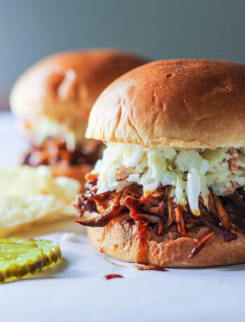 Two slow cooker BBQ pulled chicken burgers topped with coleslaw with pickles and chips.