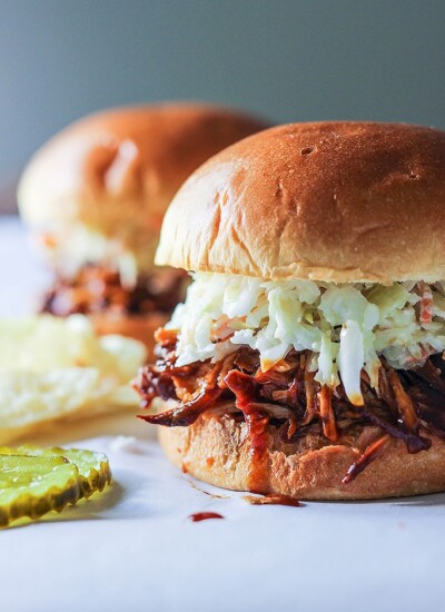 Two slow cooker BBQ pulled chicken burgers topped with coleslaw with pickles and chips.