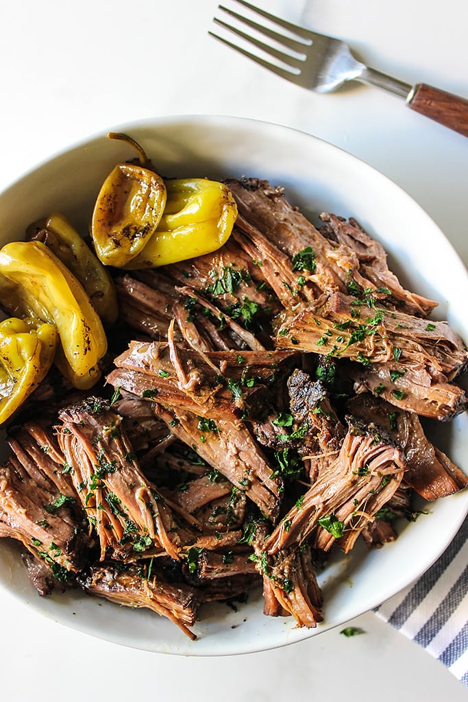 Shredded Mississippi pot roast in a bowl with pepperoncini peppers.