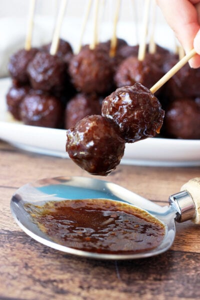 A close up shot of two sweet heat meatballs on a stick with an army of other meatballs in the background.