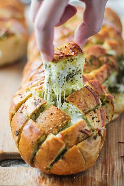 A pice of cheesy pesto pull-apart bread being pulled out with cheese strings.